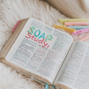 Open Bible on a soft cream blanket with the words "SOAP Study" written in colorful letters on the page, surrounded by pastel highlighters—perfect for illustrating a creative and peaceful Bible study session.